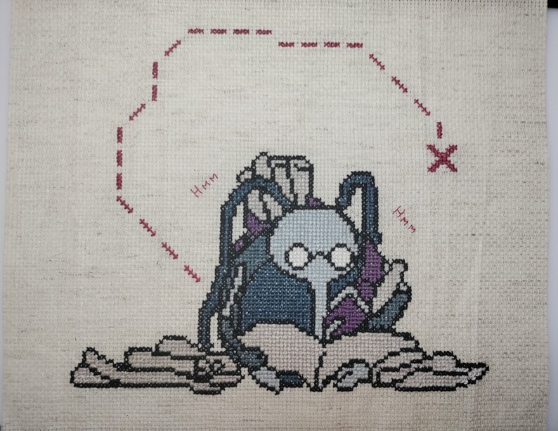 May include: Cross-stitch embroidery of a character with glasses reading a book, surrounded by scrolls. The character is wearing a blue and purple robe and has a thought bubble above their head that says "Hmm".