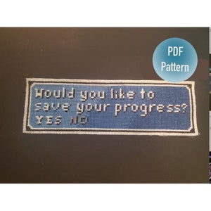 Peut inclure: Un motif de point de croix bleu et blanc représentant une invite de sauvegarde de jeu vidéo qui dit "Voulez-vous sauvegarder votre progression ? OUI NON".