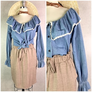 May include: A light blue denim blouse with a ruffled neckline and long sleeves, paired with a tan skirt. The blouse features white lace trim and is buttoned down the front. The skirt has a high waist and a tie.