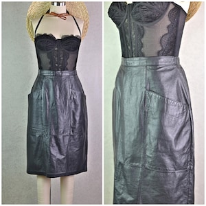 May include: Black leather skirt with a high waist and two front pockets. The skirt is paired with a black lace corset top. The outfit is displayed on a mannequin with a straw hat.