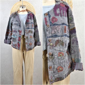 May include: A grey patchwork jacket with button fastenings and rolled-up sleeves. The jacket features embroidered elephant and floral designs in shades of purple, red, and green. The jacket is paired with beige trousers and a straw hat.