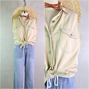 Puede incluir: Una camisa sin mangas de color beige con dos bolsillos en el pecho está anudada a la cintura. Se combina con pantalones vaqueros azul claro con bolsillos. También se ve un sombrero de paja y un collar de cuero marrón.