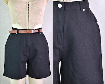 May include: Black denim shorts with a brown leather belt. The shorts have a classic design with pockets and a button closure. The belt has a silver buckle. The shorts are shown on a mannequin.