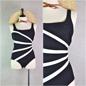 May include: A black one-piece swimsuit with white diagonal stripes. The swimsuit has a square neckline and wide straps. A straw hat with a brown leather band sits on top of the mannequin head.