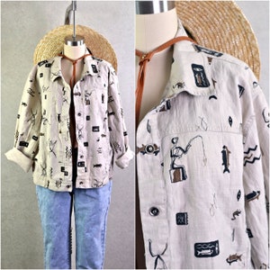 May include: Beige button-up jacket with a tribal print featuring figures, fish, and geometric shapes. The jacket has a collared neckline, buttoned cuffs, and two front pockets. The jacket is paired with light blue jeans.