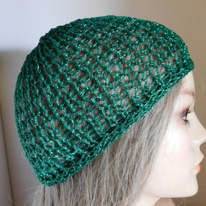 May include: A green, open-weave knit hat with a shimmering, glittery appearance. The hat is a close-fitting style, likely a beanie or cap, and is made of a net-like material. The color is a vibrant, emerald green.