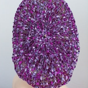 May include: A purple and silver crocheted hat with a circular design.