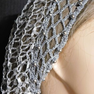 May include: A silver-colored head covering with a net-like design. The head covering is embellished with small, round, silver beads. The net-like design is made of a shiny, silver material. The head covering is likely for a special occasion.