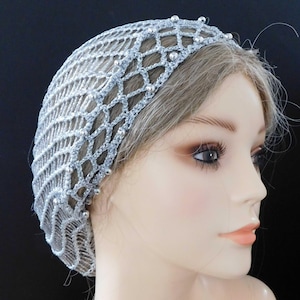 May include: A silver crocheted head covering with a net-like design. The head covering is adorned with small, silver beads along the headband. The netting covers the top of the head and extends down the back.