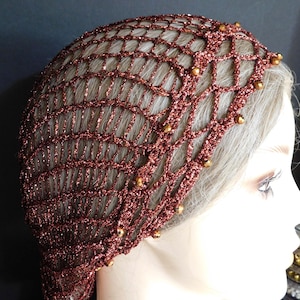 May include: A copper-colored, crocheted hair net with a net-like design. The hair net is adorned with small, gold-colored beads. The net covers the top and back of the head, and is likely used for styling or as a decorative hair accessory.
