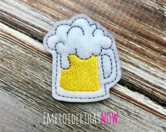 May include: White felt applique of a beer mug with yellow beer and white foam. The mug has a black outline.