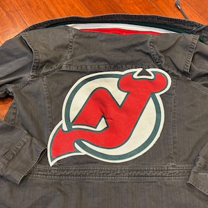 May include: A dark gray denim jacket with a large red, white, and green patch on the back. The patch features a stylized 'N' in a circle.