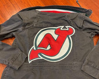 May include: A dark gray denim jacket with a large red, white, and green patch on the back. The patch features a stylized 'N' in a circle.