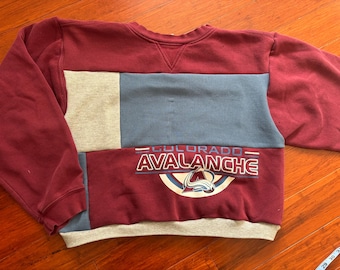 May include: A maroon, gray, and blue patchwork sweatshirt with the words "Colorado Avalanche" and a team logo printed on the front.