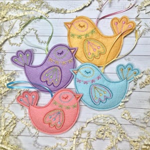 May include: Four felt bird ornaments in different colors: yellow, purple, blue, and pink. Each bird has embroidered details and a loop for hanging.