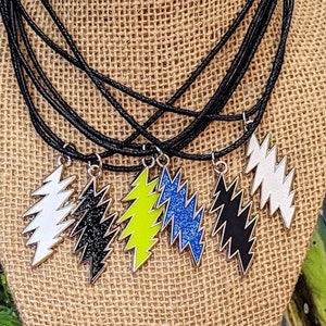 May include: Six necklaces with black cords and silver lightning bolt pendants. The pendants are in different colors: white, black, yellow, blue, and black with glitter.