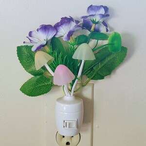 May include: A white plug-in night light with a cluster of purple flowers and green leaves. The light features four mushroom-shaped bulbs that glow in different colors.