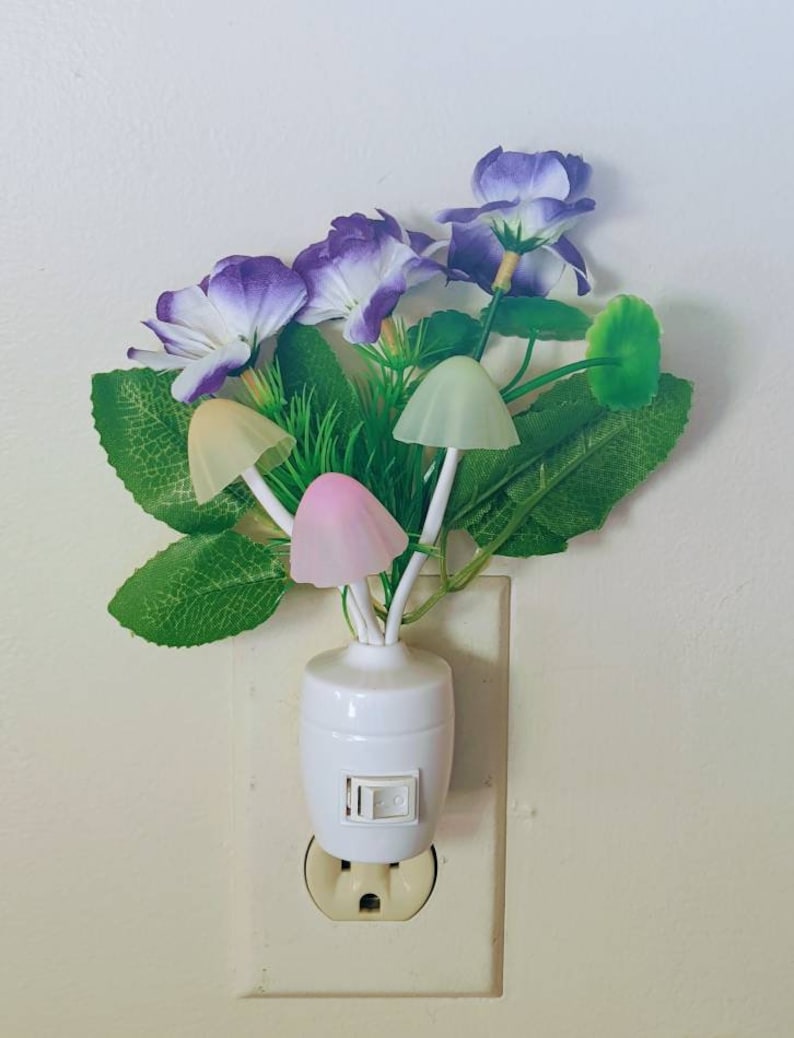 May include: A white plug-in night light with a cluster of purple flowers and green leaves. The light features four mushroom-shaped bulbs that glow in different colors.