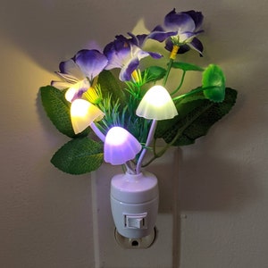 May include: A white plug-in night light with a purple flower arrangement and four mushroom-shaped LED lights. The light has a switch on the side.