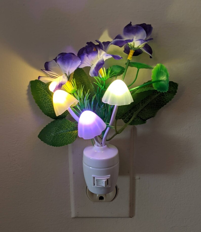 May include: A white plug-in night light with a purple flower arrangement and four mushroom-shaped LED lights. The light has a switch on the side.