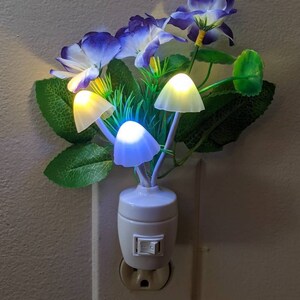 May include: A white night light shaped like a bouquet of purple flowers with glowing mushroom-shaped bulbs. The light is plugged into an electrical outlet.