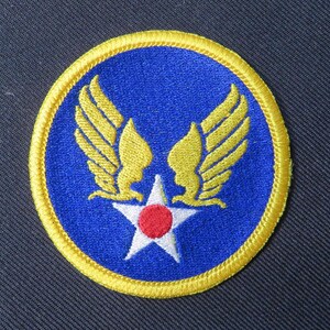 May include: A circular patch featuring a blue background with a yellow border. The patch displays a white star with a red center, flanked by two yellow wings. This patch is likely a military or aviation emblem.
