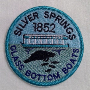 May include: A blue and white embroidered patch with the text "Silver Springs 1852 Glass Bottom Boats". The patch features a small illustration of a boat.