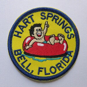 May include: A yellow and blue embroidered patch with the text "HART SPRINGS BELL, FLORIDA" and a cartoon of a person in a red inner tube.