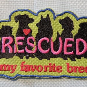 May include: Green embroidered patch with a silhouette of seven dogs, each with a red heart. The text "RESCUED is my favorite breed" is embroidered in pink.