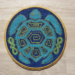May include: A blue and green embroidered patch of a turtle with a gold outline. The turtle's shell is made up of geometric shapes.