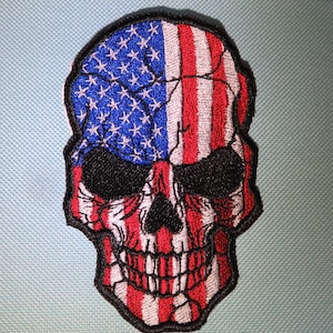 May include: Embroidered patch of a skull with the American flag design. The skull is white with black eyes and a black mouth. The flag is red, white, and blue.