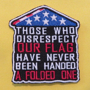 May include: A black and red embroidered patch with a house shape and the text "Those who disrespect our flag have never been handed a folded one."