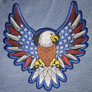 May include: Embroidered patch of a bald eagle with outstretched wings. The eagle's wings are decorated with red, white, and blue stars and stripes, resembling the American flag.