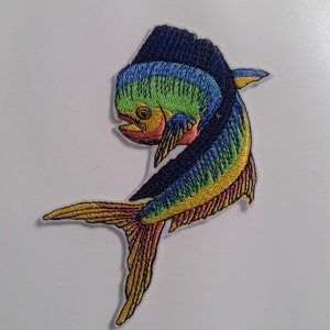 May include: A colorful embroidered patch of a dolphin jumping out of the water. The dolphin is blue, green, yellow, and red.