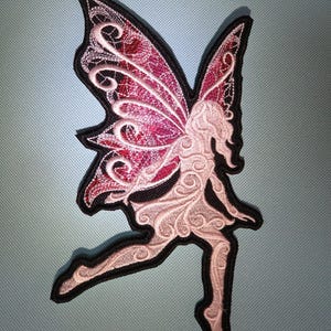 May include: Embroidered fairy patch with pink and red wings, a light pink dress, and a black outline. The fairy is in a leaping pose, with intricate details in the wings and dress.