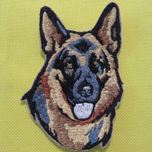 May include: Embroidered patch of a German Shepherd dog's head. The dog has brown and black fur, a black nose, and a white tongue sticking out. The patch is on a green background.