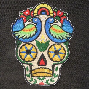 May include: Embroidered sugar skull patch with colorful flowers, green leaves, and two blue birds with yellow, green, and red accents.