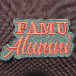 May include: A teal blue embroidered patch with the text "FAMU Alumni" in red lettering.