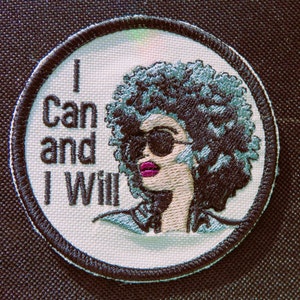 May include: White embroidered patch with a black outline. The patch features a woman with an afro wearing sunglasses and a pink lipstick. The text "I Can and I Will" is embroidered in black.
