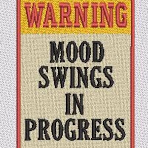May include: A rectangular embroidered patch with a red border. The top section features a yellow background with the red text WARNING. The lower section has a beige background with the black text MOOD SWINGS IN PROGRESS, all stitched on fabric.