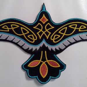May include: A black embroidered iron-on patch of a stylized bird with gold and turquoise details. The bird has a Celtic knot design on its wings and tail.
