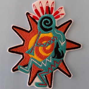 May include: Embroidered patch featuring a Native American flute player in turquoise, with a black wolf silhouette, set against a sunburst design in orange, yellow, and red. The patch has a white border.