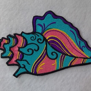 May include: A colorful embroidered seashell patch with a turquoise, pink, purple, and yellow design. The patch is outlined in black.
