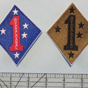 May include: Two embroidered patches, one blue with white stars and red lettering, the other brown with white stars and black lettering. Both patches feature the number "1" and the text "GUADALCANAL".