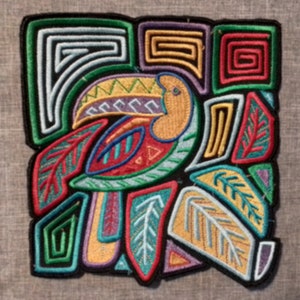 May include: Embroidered patch featuring a colorful toucan design. The toucan has a yellow beak, red and green feathers, and is surrounded by geometric shapes in green, purple, and yellow. The patch is outlined in black.