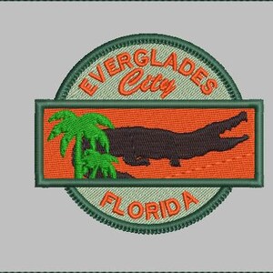 May include: Embroidered patch featuring a stylized alligator silhouette and palm tree against an orange background. The patch is framed by a green border with the words "EVERGLADES City FLORIDA" in orange and green lettering.