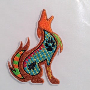 May include: Embroidered patch of a colorful wolf howling with a paw print on its back. The wolf is outlined in brown and has a green, orange, and blue patterned design.