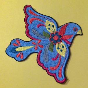 May include: A blue embroidered patch of a stylized bird with red, yellow, green, and gray floral details.