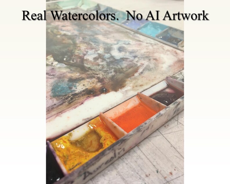 May include: A close-up of a watercolor paint palette with four wells. The wells contain orange, yellow, and dark purple paint. The palette is made of white plastic and has a worn, used appearance. The text "Real Watercolors. No AI Artwork" is visible at the top of the image.
