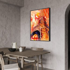 May include: A watercolor painting of the Eiffel Tower in Paris, France. The painting is in shades of orange, yellow, and red, with a blue sky in the background. The painting is framed in a black frame and is hanging on a wall in a dining room.
